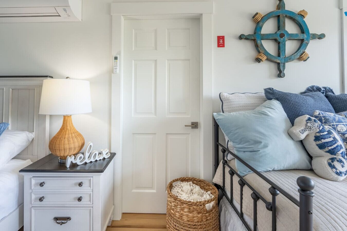 Une chambre à coucher avec un lit, une table de chevet avec une lampe, un panier et un gouvernail de bateau fixé au mur.