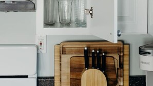 Een keuken met een inbouwkast vol glazen, een houten snijplank met messen, en een koffiezetapparaat.