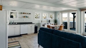 Een moderne keuken met witte kastjes, een eethoek met een tafel en stoelen, en een groot raam met uitzicht op een terras.
