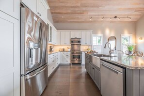 A modern kitchen with stainless steel appliances, white cabinetry, and a wooden ceiling.