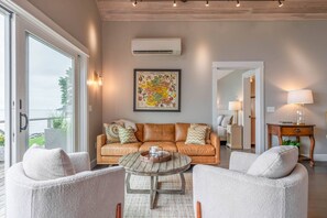 Een woonkamer met een leren bank, twee fauteuils, een houten salontafel en een grote ingelijste botanische afbeelding aan de muur.