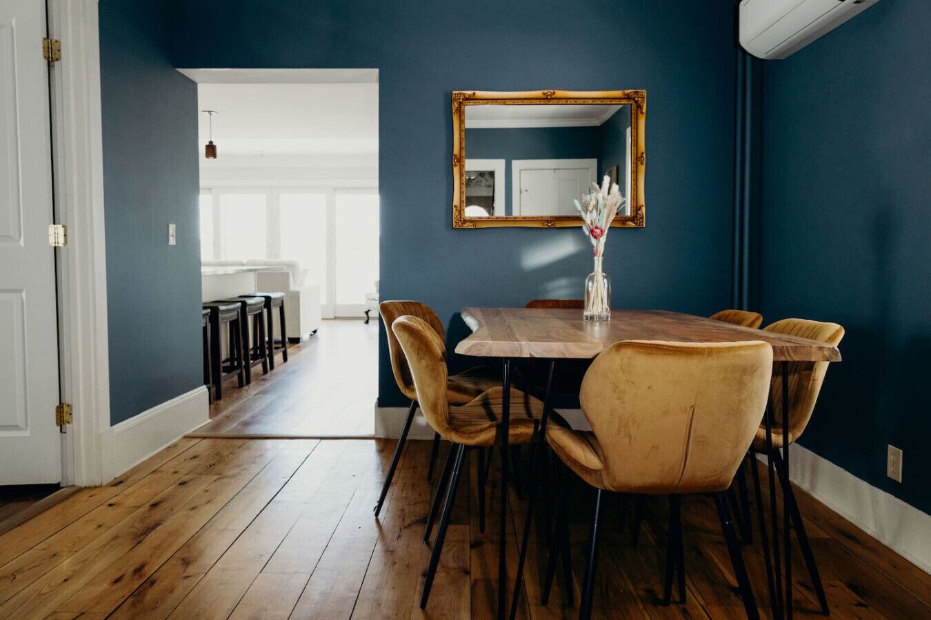 Un coin repas avec une table et des chaises en bois, un miroir au mur et un vase rempli de fleurs.