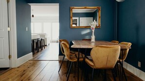 A dining area with a wooden table and chairs, a mirror on the wall, and a vase with flowers.