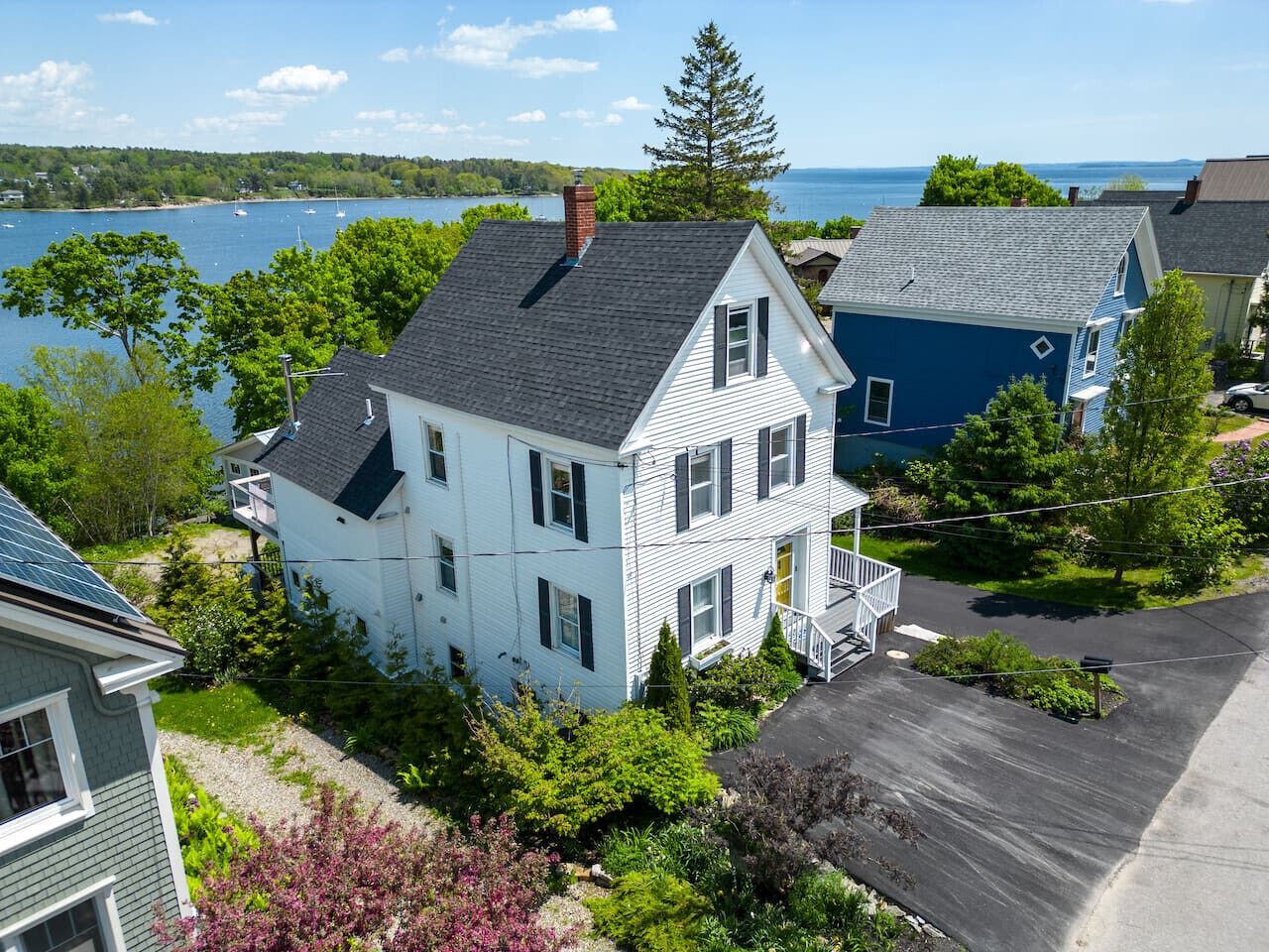 Une maison à deux étages, dotée d’un porche à l’avant et d’un garage, entourée d’une végétation luxuriante et offrant une vue sur un lac.