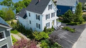 A two-story house with a front porch and a garage, surrounded by lush greenery and a view of a lake.