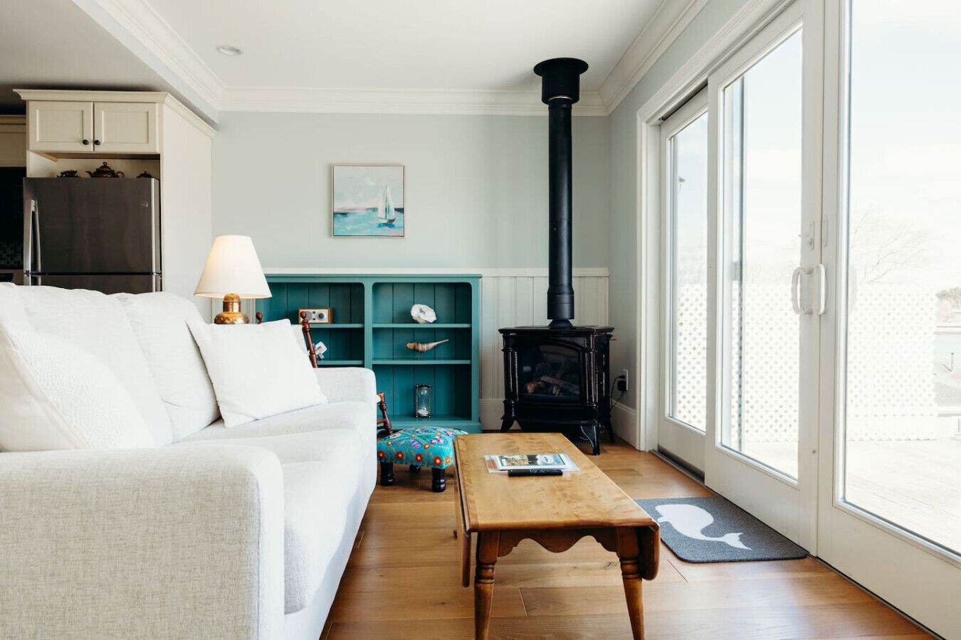 Un salon chaleureux avec un canapé blanc, une table basse en bois, une étagère turquoise et un poêle à bois noir.