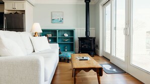 A cozy living room with a white sofa, a wooden coffee table, a teal shelving unit, and a black wood-burning stove.