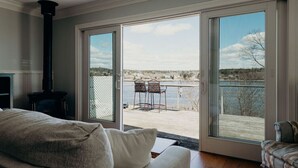 A living room with a large sliding glass door leading to a deck with a view of a lake and trees.
