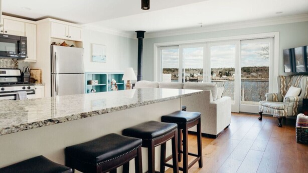 A modern kitchen with a large island, bar stools, and a view of the outdoors through large windows.