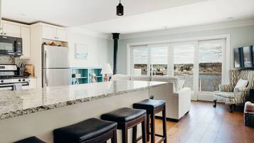 Une cuisine moderne dotée d’un grand îlot central, de tabourets de bar et offrant une vue sur l’extérieur grâce à de grandes fenêtres.