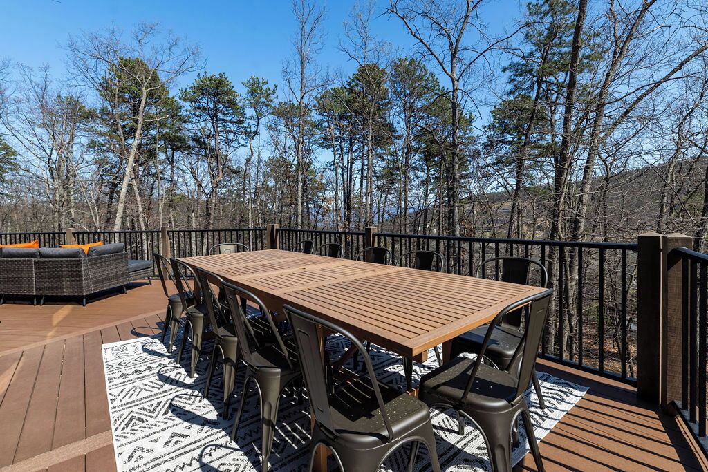 A wooden deck with a table and chairs, surrounded by a railing and trees.