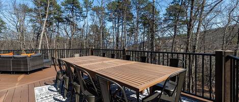 A wooden deck with a table and chairs, surrounded by a railing and trees.