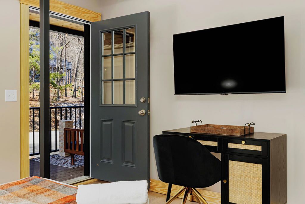A room with a dark grey door, a black chair, a small wooden table, and a mounted TV.