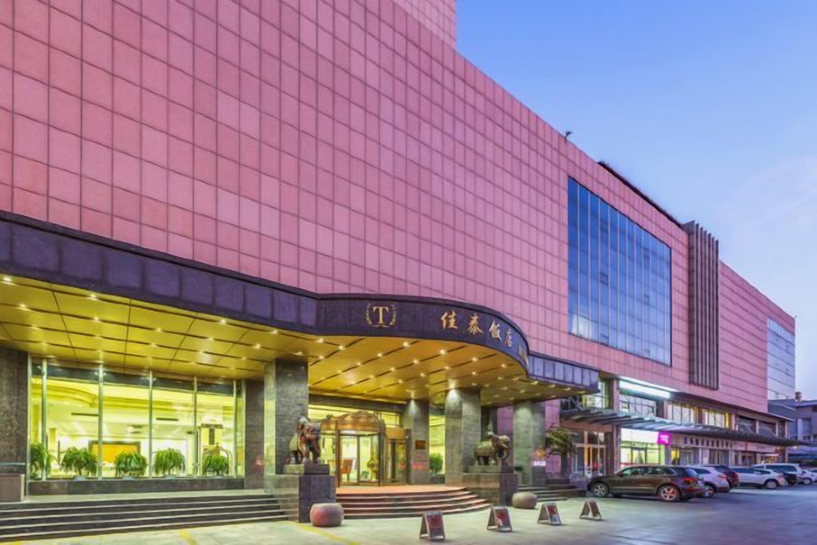 A modern hotel with a prominent entrance, large windows, and a parking area.