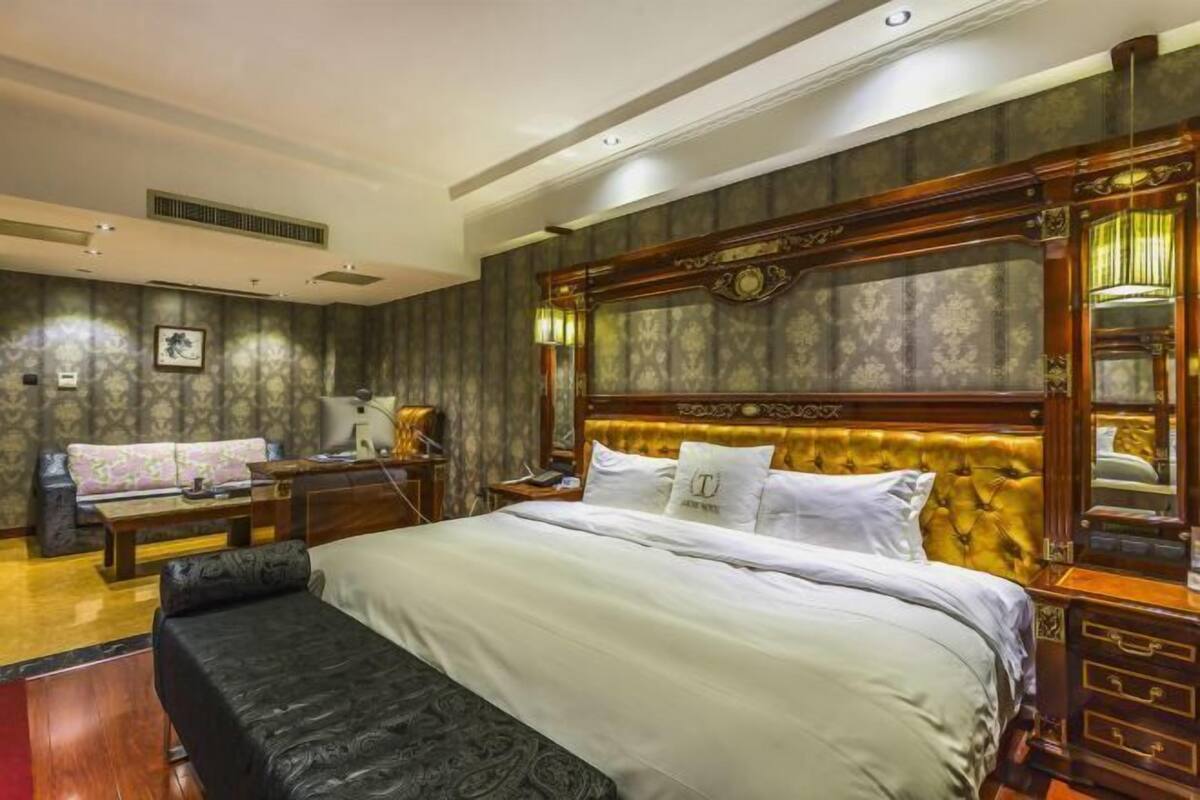 A bedroom with a large bed, a sofa, a desk, and a mirror.