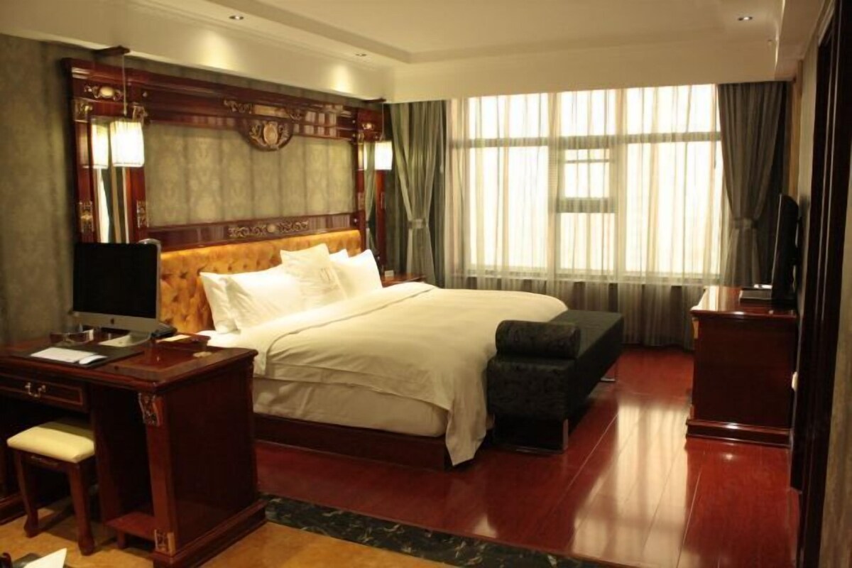 A hotel room with a large bed, a desk with a chair, a television, and a window with curtains.