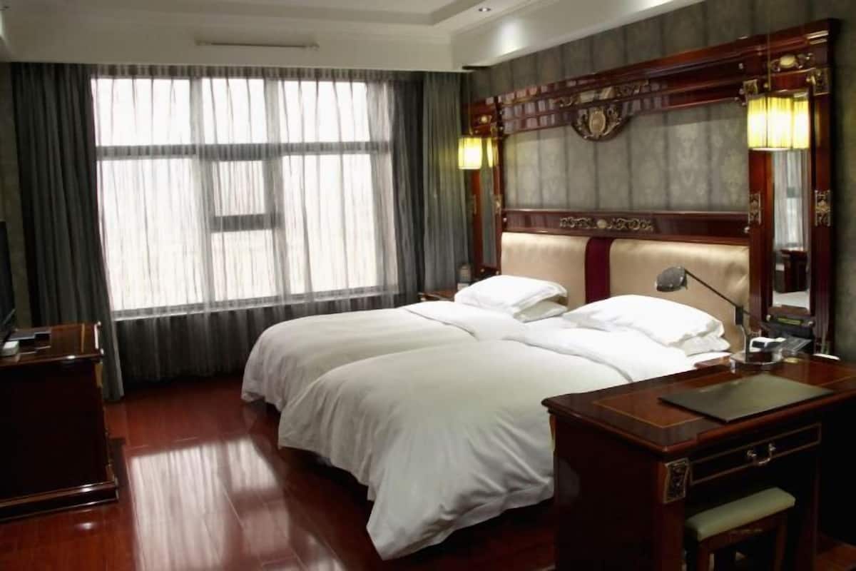 A hotel room with a large bed, a desk, a chair, a lamp, and a mirror.