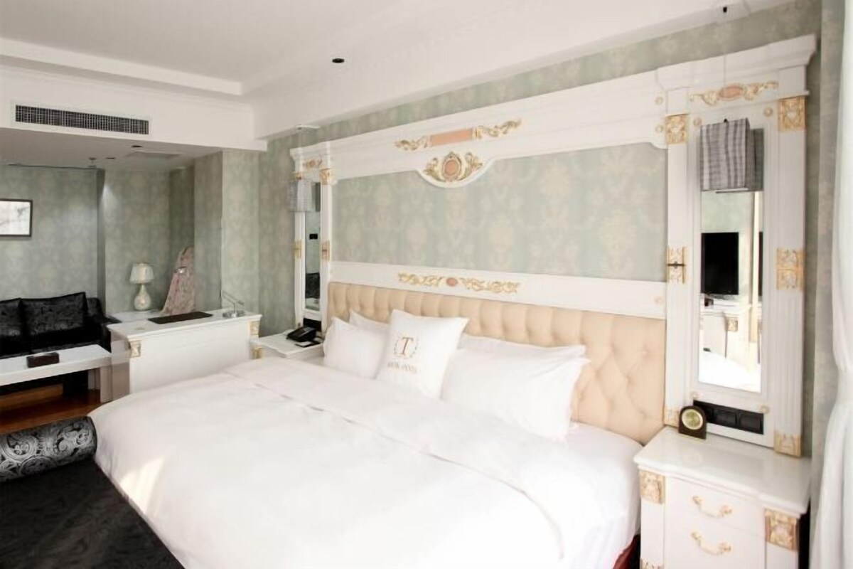 A bedroom with a large bed, a nightstand, a dresser, and a mirror.