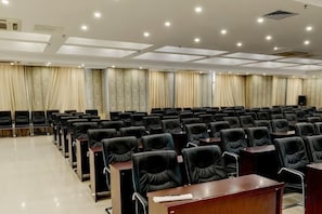 A conference room with rows of chairs and tables, a stage with curtains, and a ceiling with recessed lighting. - Jiatai Hotel (Binzhou)