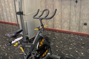 A stationary exercise bike with a black and yellow color scheme, positioned in a room with a patterned wall and a tiled floor. - Jiatai Hotel (Binzhou)