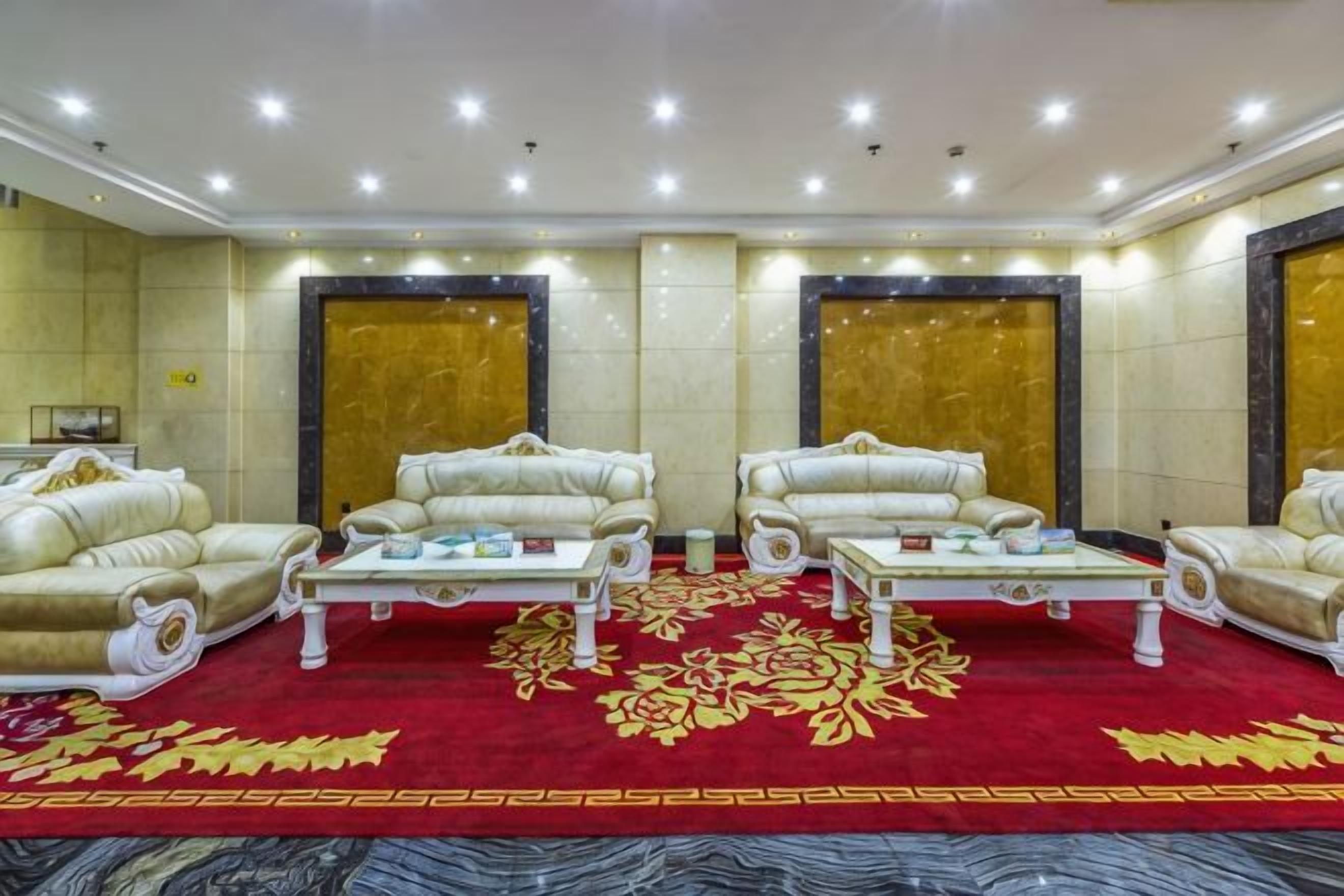 Quarto de hotel com carpete vermelho, dois sofás, uma mesa de centro e um espelho grande.