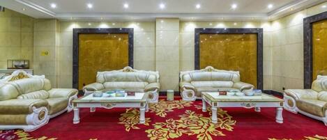 Quarto de hotel com carpete vermelho, dois sofás, uma mesa de centro e um espelho grande.