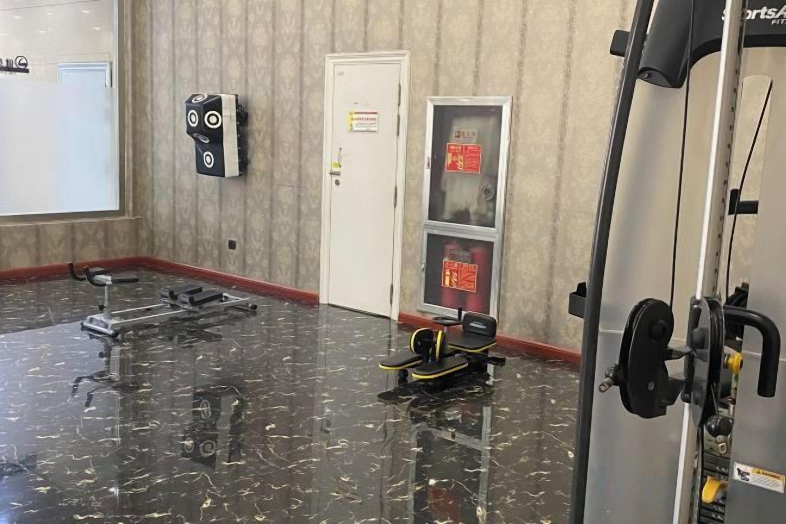 A gym with exercise equipment, a door with a sign, and a wall-mounted device.