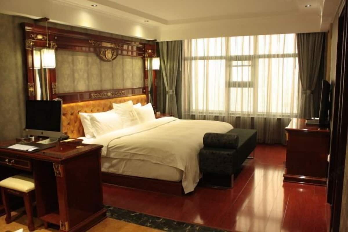 A hotel room with a large bed, a desk, a chair, a television, and a window with curtains.