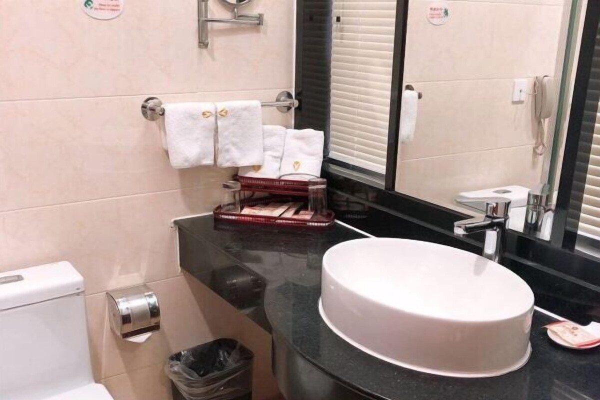 A bathroom with a round sink, a toilet, and a mirror. There are towels hanging on a rack and a trash bin.