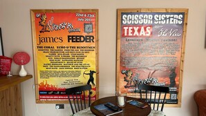 Ein Essbereich mit Tisch und Stühlen, einem Poster an der Wand und einem roten Gegenstand auf einem Regal.