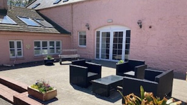 Ein pinkfarbenes Gebäude mit einer Terrassenfläche, die Sitzgelegenheiten und Pflanzgefäße im Freien bietet.