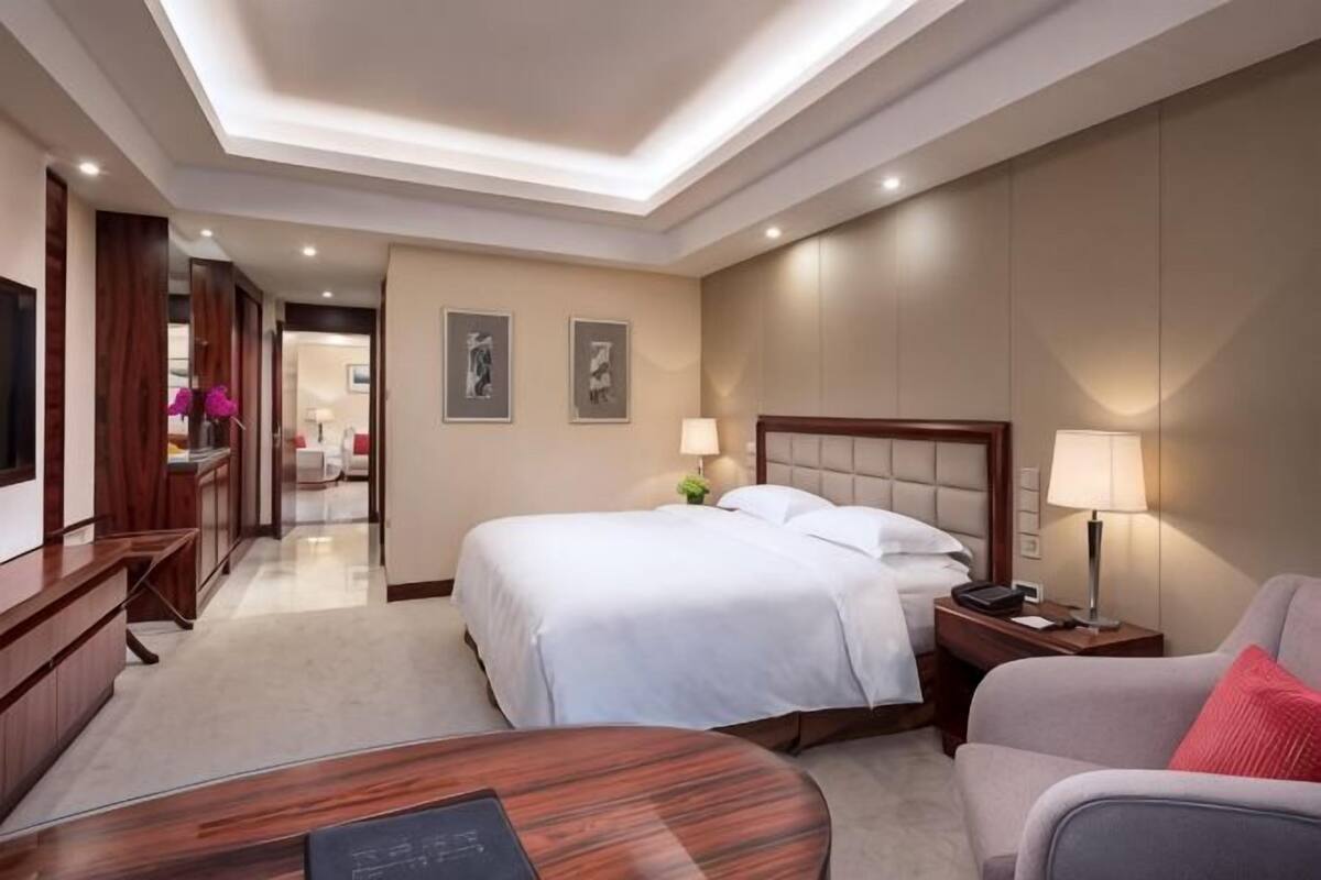 A hotel room with a bed, bedside tables, a desk, a chair, and a TV.