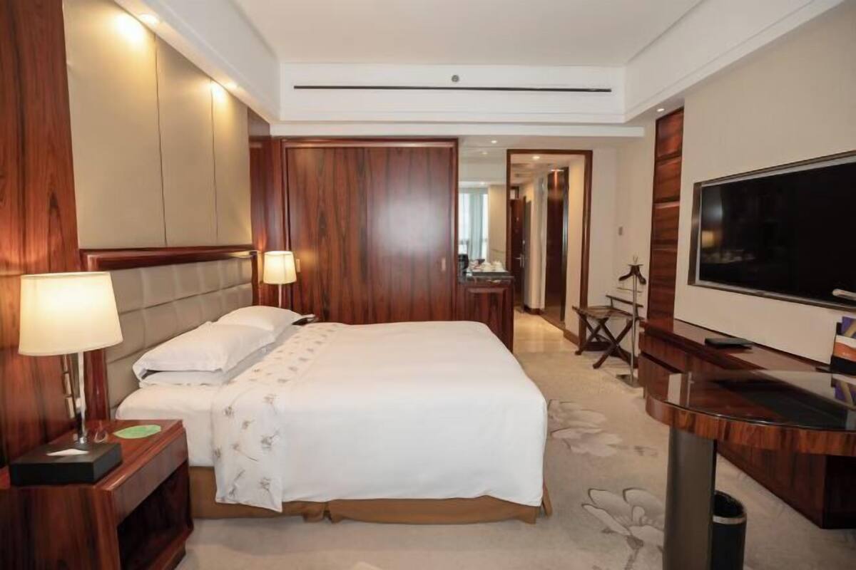 A hotel room with a large bed, a TV, a desk, and a mirror.