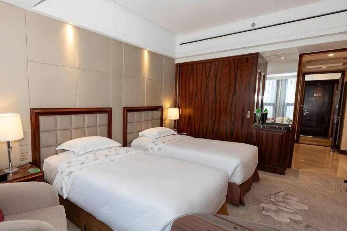 A hotel room with two beds, a desk, and a mirror.