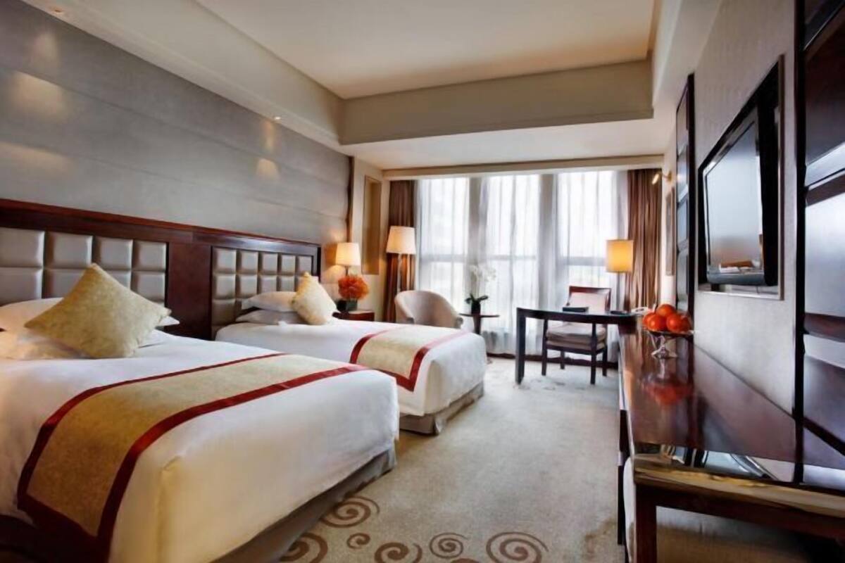 A hotel room with two beds, a desk, a chair, and a large window.