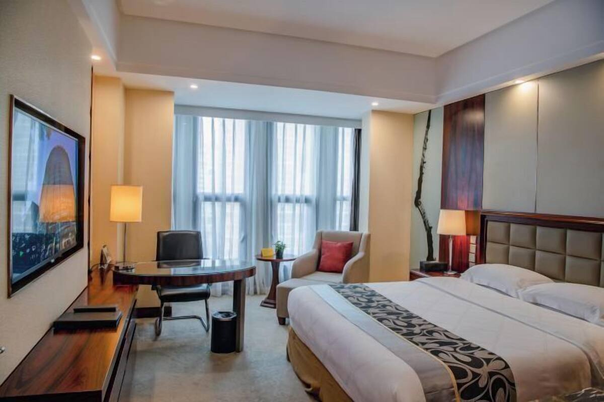 A hotel room with a bed, desk, chair, and a large window with curtains.