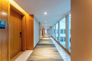 Un pasillo de hotel con puertas de madera, alfombra estampada y ventanas amplias.