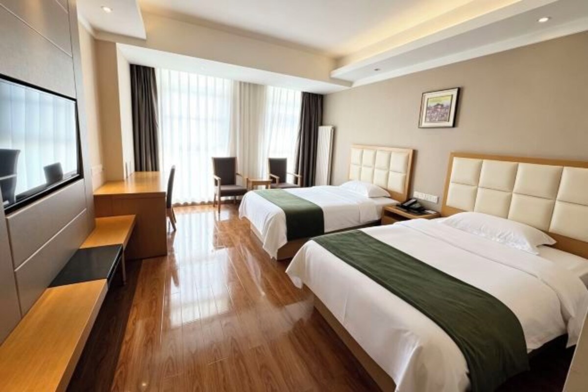 A hotel room with two beds, a desk, and a TV.