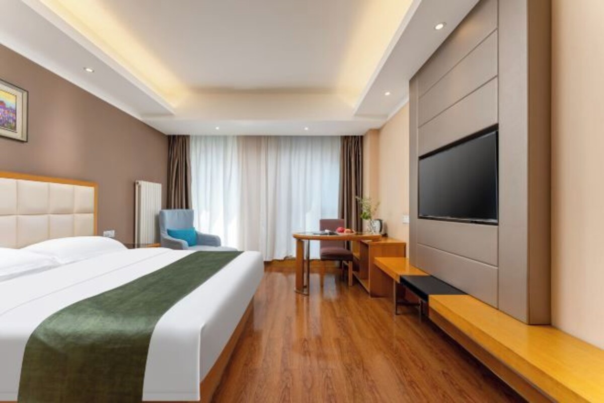 A hotel room with a bed, a desk, a chair, a TV, and a window with curtains.