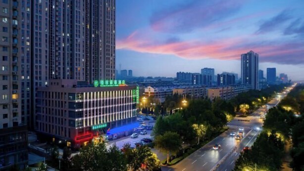 A high-rise building with a modern design, surrounded by a well-lit urban street at dusk. - GreenTree Inn (Feicheng Xincheng Road) (Feicheng)