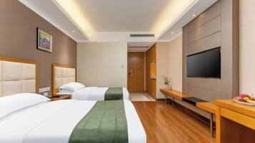 A hotel room with two beds, a flat-screen TV, a desk, and a small table with fruit.