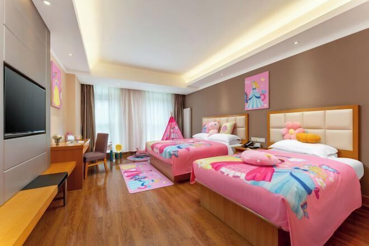 Habitación de hotel con dos camas, un escritorio, una silla, un televisor y una ventana con cortinas.