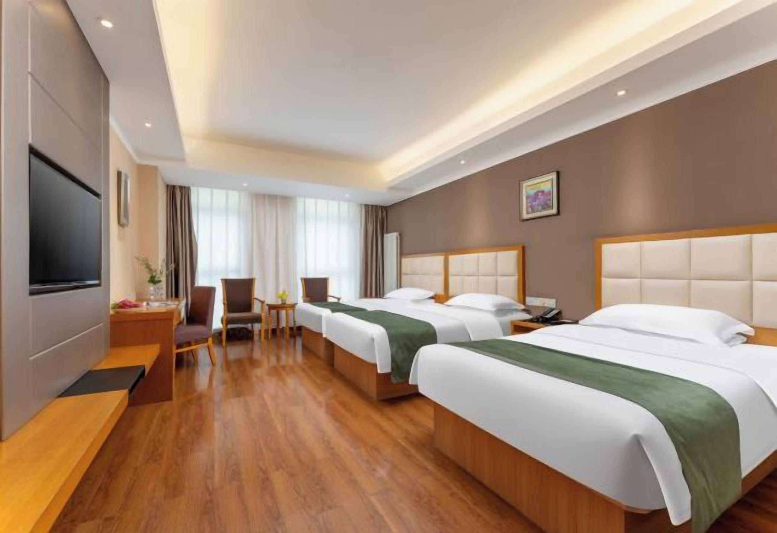 A hotel room with two beds, a desk, a chair, a TV, and a window with curtains.