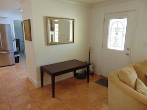 A living room with a dark wooden bench, a guitar, a mirror, and a door with a stained glass window.