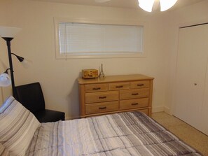 A bedroom with a bed, a dresser, a chair, a lamp, and a window with blinds.