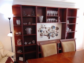 A dining area with a wooden table and chairs, surrounded by shelves with glassware and decorative items.
