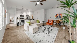 A modern living room with a white sofa, a glass coffee table, and a dining area with a wooden table and chairs. - Stylish 2BR Apartment! Pool, Gym & Prime Location Near Downtown & Airport (Austin)