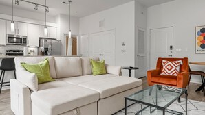 A modern living room with a white sectional sofa, a glass coffee table, and an orange armchair. - Stylish 2BR Apartment! Pool, Gym & Prime Location Near Downtown & Airport (Austin)