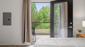 A bedroom with a large bed, a sliding glass door to a balcony, and a view of greenery outside. - Stylish 2BR Apartment! Pool, Gym & Prime Location Near Downtown & Airport (Austin)