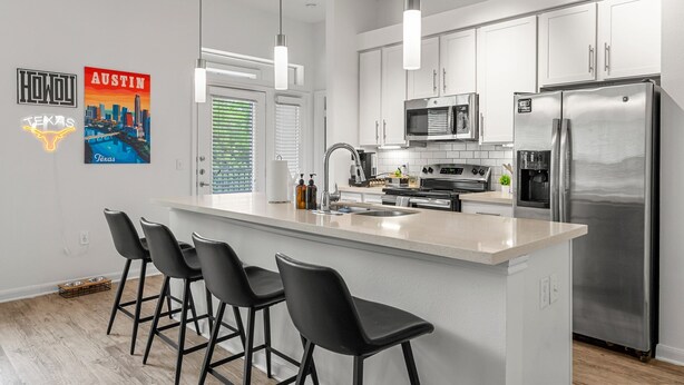 A modern kitchen with a central island, stainless steel appliances, and black bar stools. - Stylish 2BR Apartment! Pool, Gym & Prime Location Near Downtown & Airport (Austin)